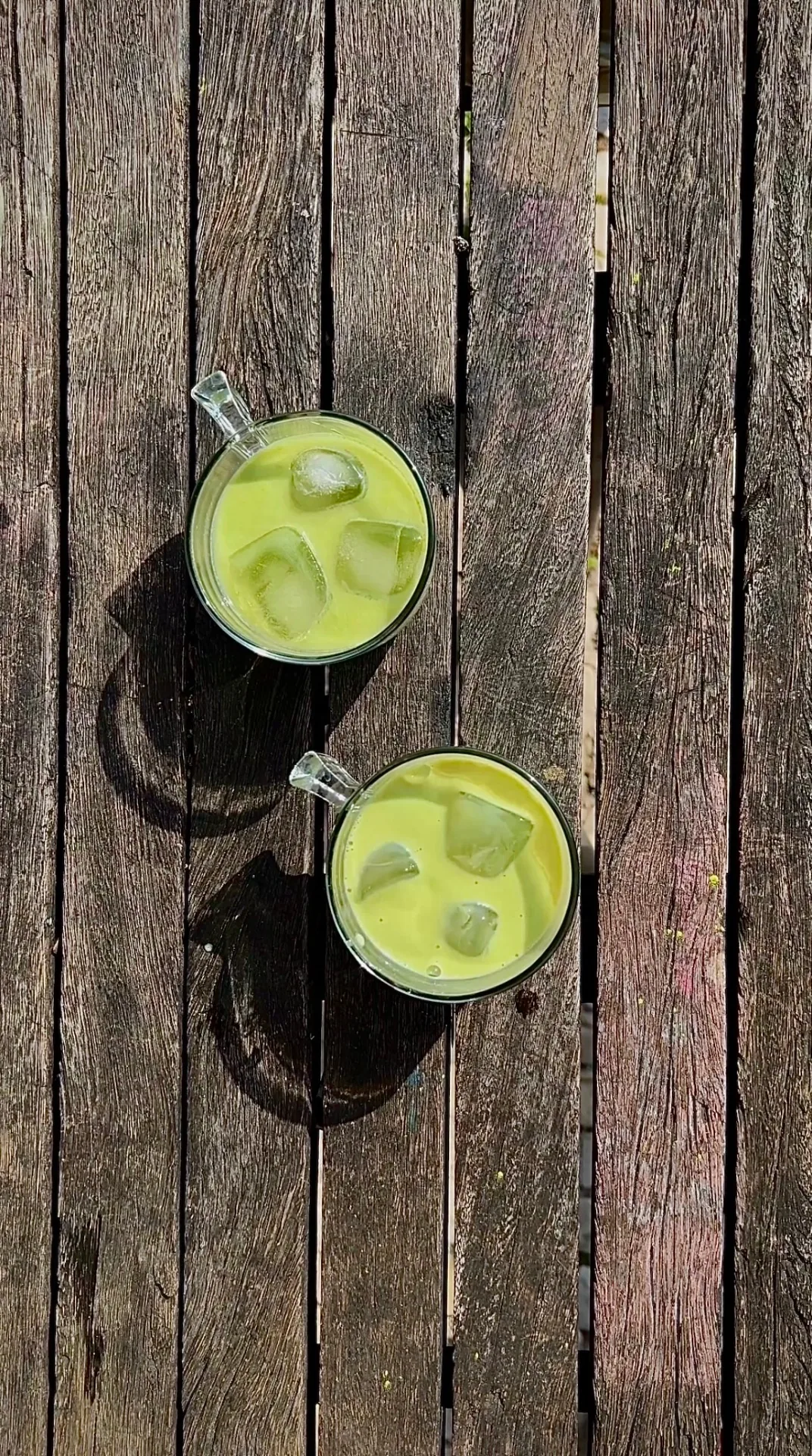 Two iced green rooibos lattes on a wooden deck